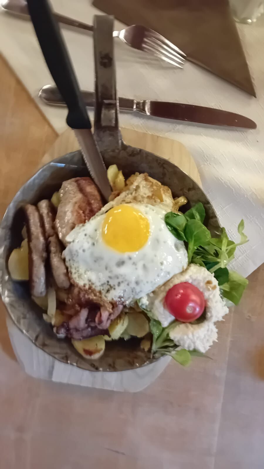 Poêlon garni de pommes de terre sautées, de saucisses, de viande grillée, d'un œuf au plat et de mâche