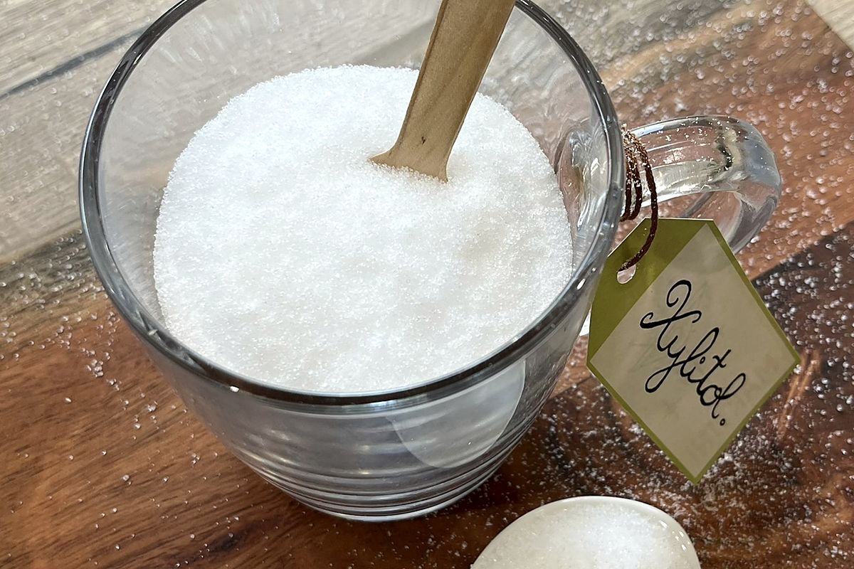 Tasse en verre remplie de xylitol vue de dessus, un bâtonnet en bois planté dedans et une étiquette manuscrite attachée à l'anse