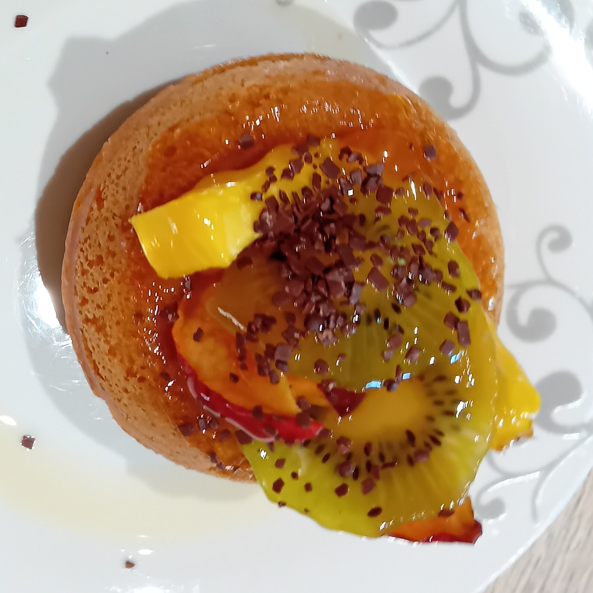 Baba au rhum imbibé de sirop au xylitol, garni de kiwi, d'ananas et de nectarine, parsemé de masse de cacao râpée, vu du dessus