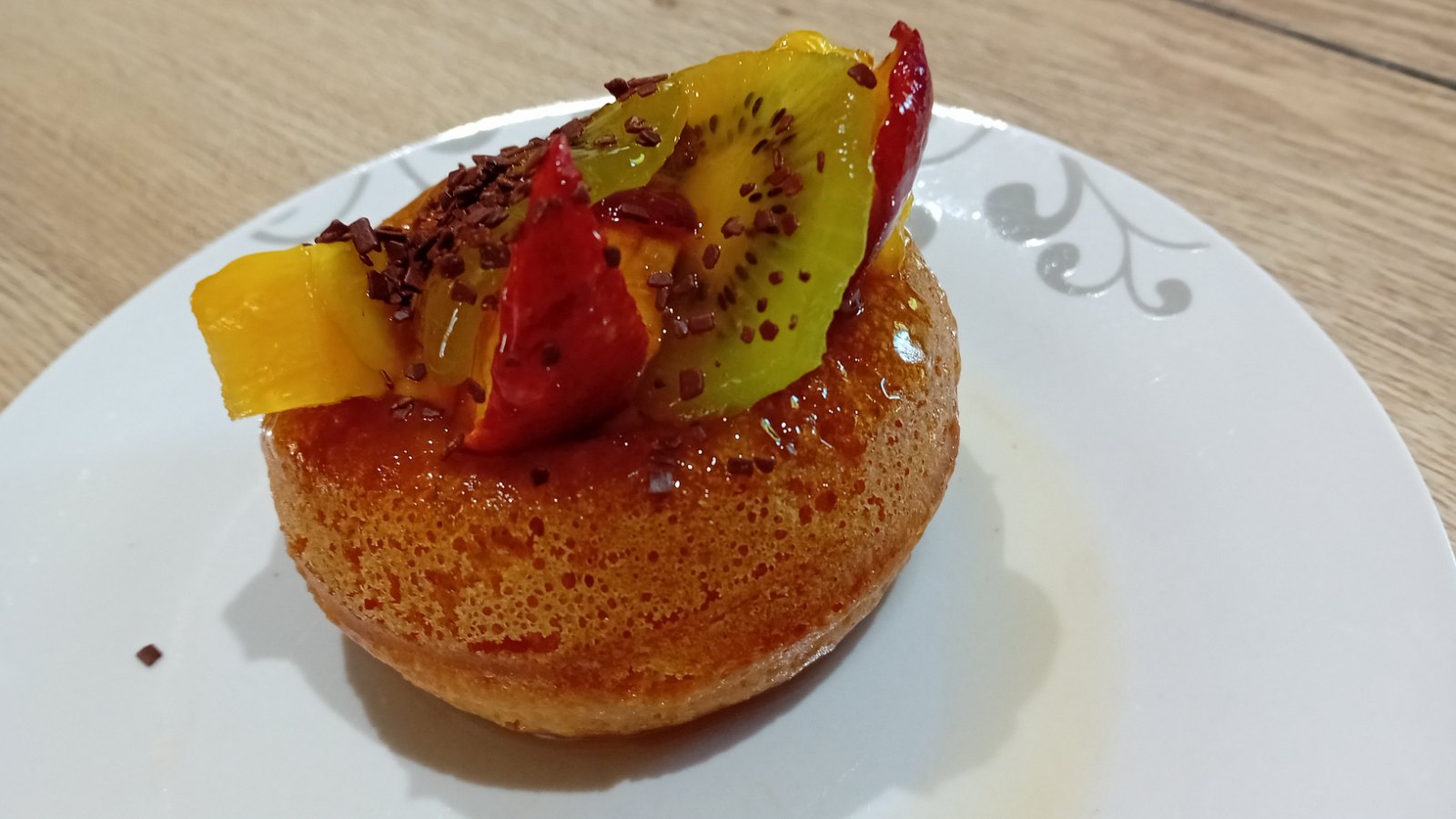 Baba au rhum imbibé de sirop au xylitol, garni de kiwi, d'ananas et de nectarine, parsemé de masse de cacao râpée
